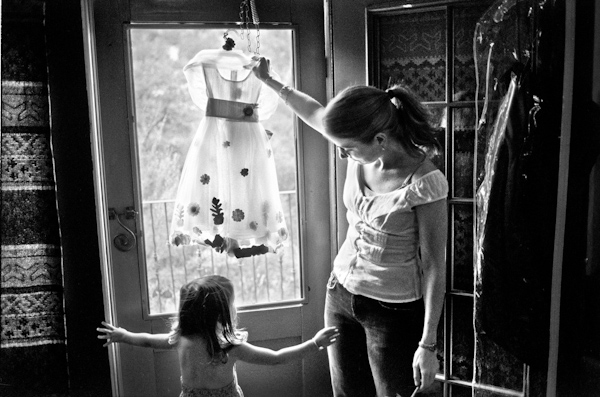 black and white photo of a mom and her daughter, the flower girl,  looking up at the flower girl's dress as it hangs from the door window  - photo by New Mexico based wedding photographers Twin Lens